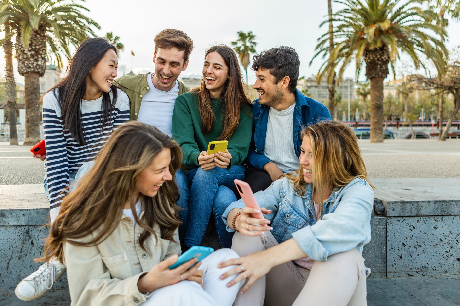 Happy group of student people with mobile phones having fun sitting outdoors